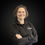 Lächelnde Person in schwarzer Jacke vor schwarzem Hintergrund.